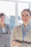 Happy businesswomen with arms crossed smiling at camera by large window