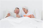 Mature man showing his newspaper to his wife in bed