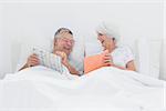 Cheerful woman showing her book to husband in bed