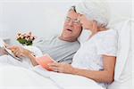 Mature couple looking at a newspaper in bed
