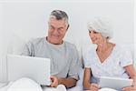 Mature man showing something on his laptop to his wife on bed