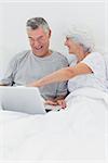 Mature woman pointing at husbands laptop in bed
