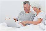 Mature man with wife pointing at a laptop in bed