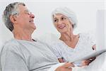 Cheerful mature couple using a laptop together in bed