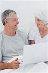 Cheerful mature couple using a laptop in bed
