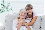 Little girl hugging her grandmother sitting on the couch