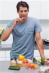 Attractive man eating a slice of bell pepper in the kitchen
