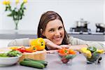 Cheerful woman leaning on the counter of her kitchen with vegetables on it