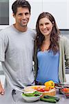 Cheerful couple smiling at camera and preparing vegetables in their kitchen