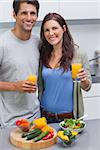 Delighted couple holding glass of orange juice in the kitchen