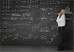 Elegant businessman looking at maths equations written on a blackboard
