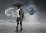 Businessman looking at earth projection and holding his umbrella and jacket