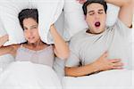 Woman covering ears with a cushion while her partner is snoring next to her