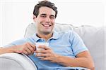 Portrait of a cheerful man holding a cup of coffee sat on a couch