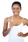 Smiling woman with hand on hip holding her toothbrush on white background