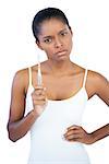 Serious woman with hand on hip holding her toothbrush on white background