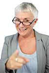 Woman with glasses pointing at camera on white background