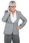 Furious businesswoman calling someone with her hand on hip on white background