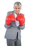 Serious businesswoman standing with her boxing gloves on white background