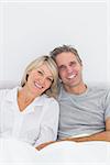 Smiling couple in bed looking at camera