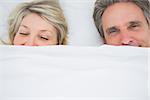 Couple waking up under the covers at home in bed
