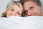 Couple smiling from under the covers at home in bed
