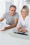 Cheerful couple using laptop in the morning sitting at kitchen counter
