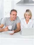 Content couple using laptop in the morning sitting at kitchen counter