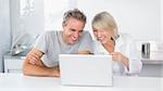 Happy couple laughing at laptop in the morning sitting at kitchen counter