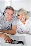 Smiling couple using their laptop in the morning looking at camera sitting at kitchen counter