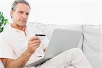 Man on his couch using laptop for online shopping at home in living room