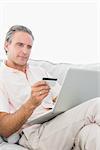 Man on his couch using laptop for shopping online at home in living room