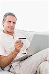 Man on his couch using laptop for shopping online smiling at camera at home in living room