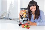 Happy brunette with juicer full of fruit at home in kitchen