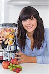 Smiling brunette with juicer full of fruit at home in kitchen