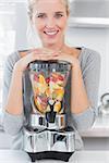 Blonde woman leaning on her juicer full of fruit at home in kitchen