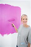 Happy blonde painting her wall pink and smiling at camera in new home