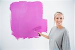 Happy young woman painting her wall pink and smiling at camera