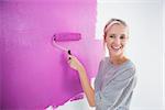 Laughing woman painting her wall in pink and looking at camera