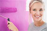 Smiling woman painting her wall in pink and looking at camera