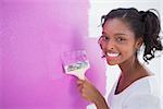 Happy young woman painting her wall in pink and smiling at camera