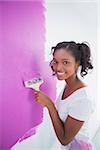 Cheerful young woman painting her wall in pink and looking at camera