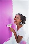 Laughing young woman painting her wall in pink and smiling at camera