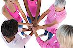 Group wearing pink and ribbons for breast cancer with hands together on white background