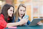 Pre-teen girls looking at cell phone and tablet computer, outdoors