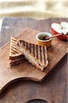 Grilled Cheese Panini with Cheddar and Apple Cut in Half on Cutting Board with half a Red Apple and Dijon Mustard in small Bowl, Studio Shot