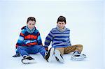 Two boys with ice-skates sitting on a frozen lake