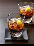 Table with 2 glasses of whisky and cola garnished with lemon