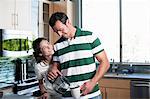 Young couple pouring coffee from pot in kitchen, smiling