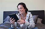 Young woman sitting bed reading electronic book, smiling